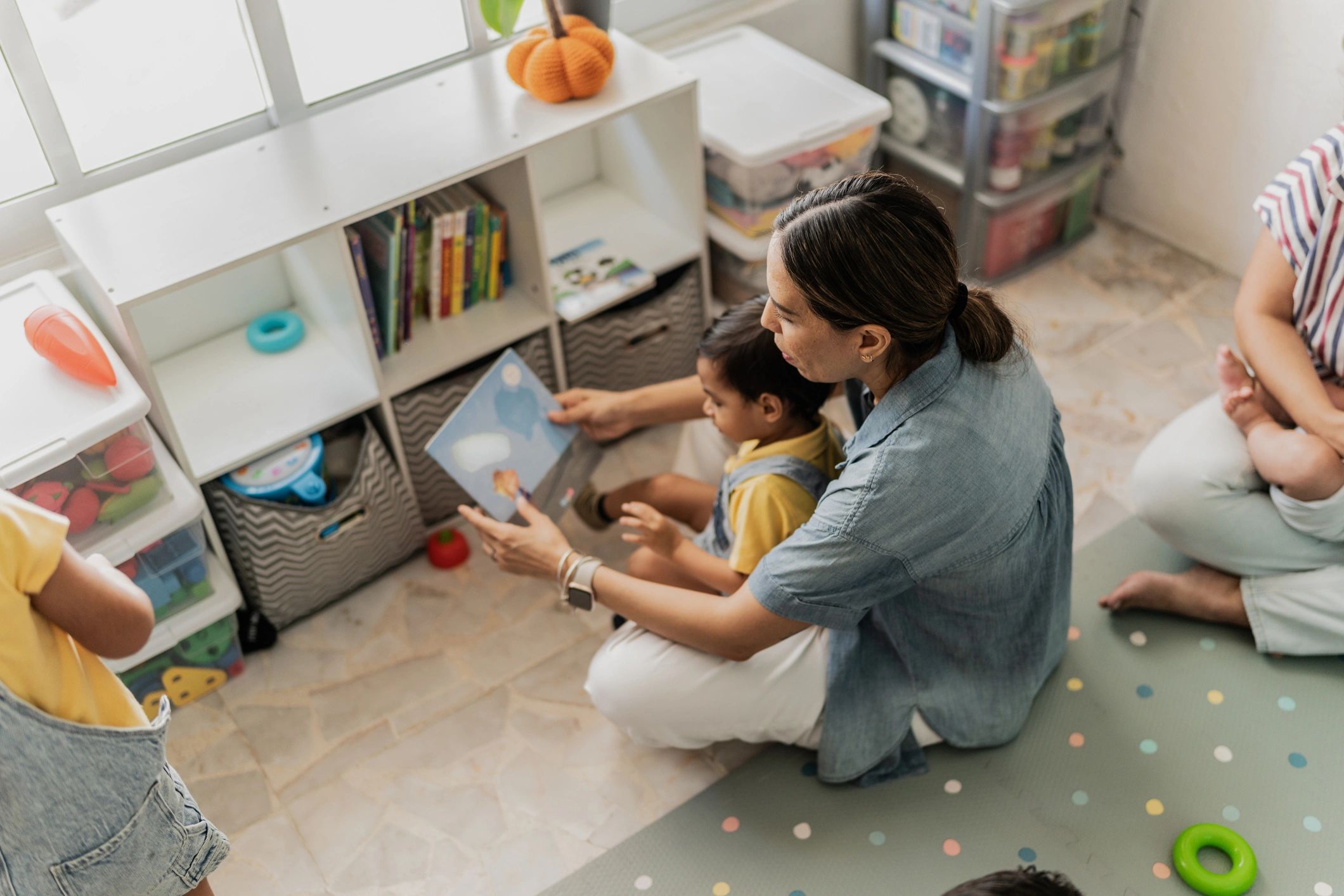 Caregiver reading a book with a child in a playroom
